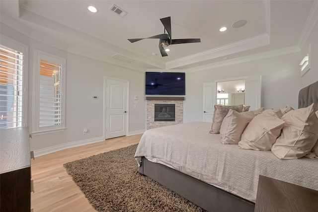 bedroom with light hardwood / wood-style floors, a fireplace, ceiling fan, a raised ceiling, and crown molding