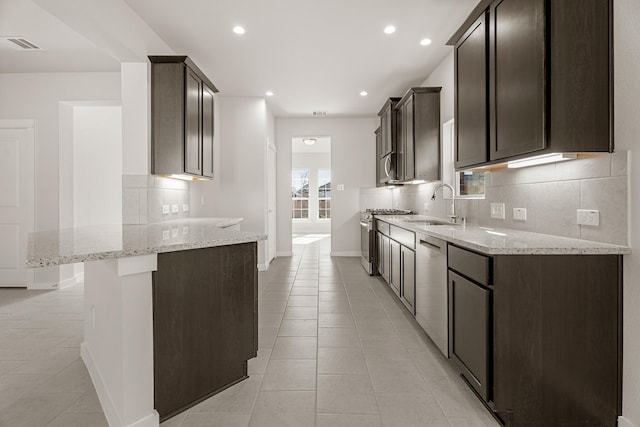 kitchen with sink, decorative backsplash, light tile patterned floors, light stone counters, and stainless steel appliances