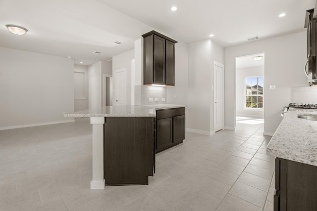 kitchen featuring light stone counters, light tile patterned floors, and dark brown cabinetry