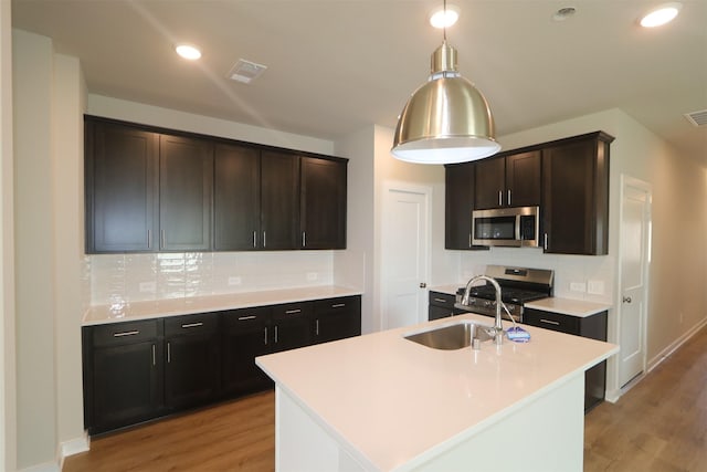 kitchen with appliances with stainless steel finishes, a kitchen island with sink, light hardwood / wood-style floors, and sink