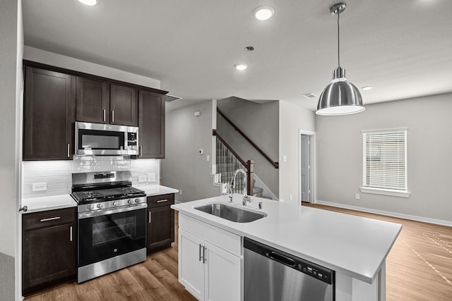 kitchen with sink, backsplash, stainless steel appliances, a kitchen island with sink, and white cabinets