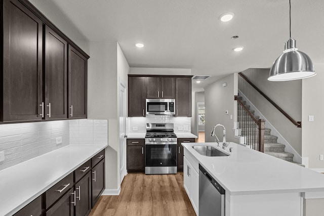 kitchen with sink, appliances with stainless steel finishes, hanging light fixtures, tasteful backsplash, and light wood-type flooring