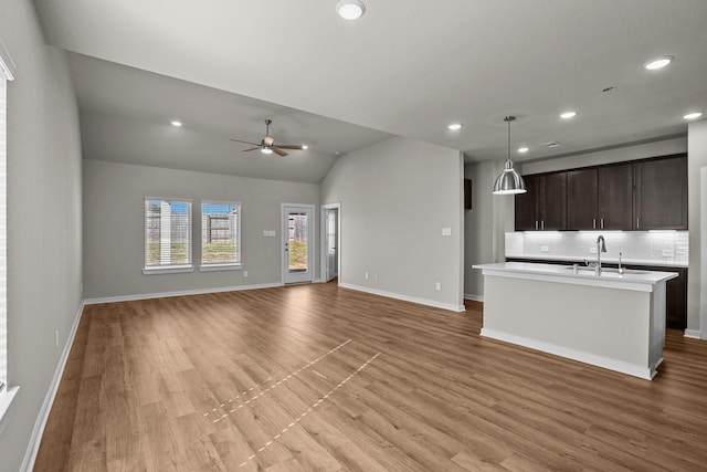 kitchen with vaulted ceiling, pendant lighting, an island with sink, decorative backsplash, and dark brown cabinetry