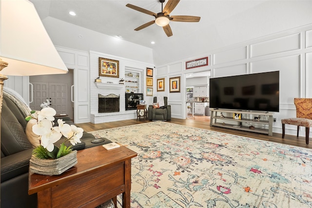 living room with a brick fireplace, built in features, ceiling fan, and wood-type flooring