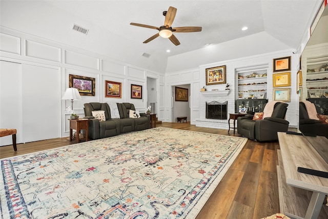 living room featuring built in shelves, ceiling fan, dark hardwood / wood-style floors, and a brick fireplace