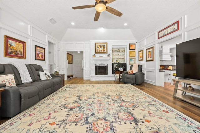 living room with a brick fireplace, built in shelves, ceiling fan, and vaulted ceiling