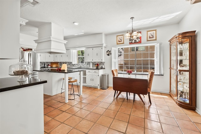 kitchen with a kitchen breakfast bar, a textured ceiling, white cabinets, a chandelier, and light tile patterned flooring