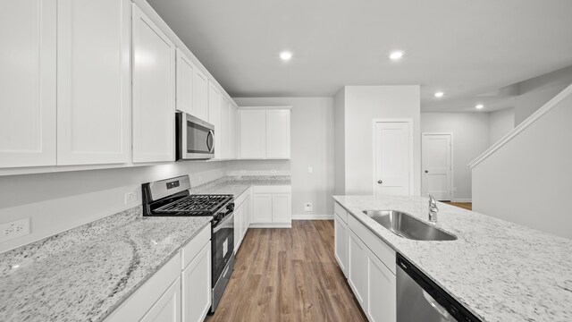 kitchen featuring white cabinets, appliances with stainless steel finishes, light hardwood / wood-style floors, sink, and light stone counters