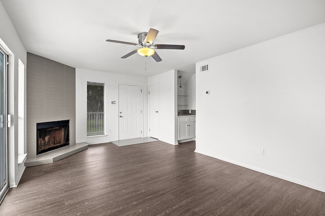 unfurnished living room featuring dark hardwood / wood-style flooring, ceiling fan, and a large fireplace