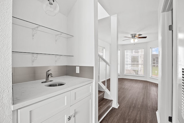 bar with light stone countertops, white cabinetry, sink, ceiling fan, and dark wood-type flooring