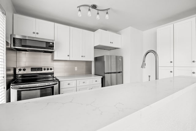 kitchen featuring tasteful backsplash, light stone counters, stainless steel appliances, sink, and white cabinetry