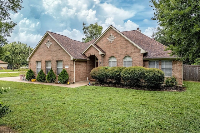 view of front of home featuring a shingled roof, a chimney, a front lawn, and brick siding