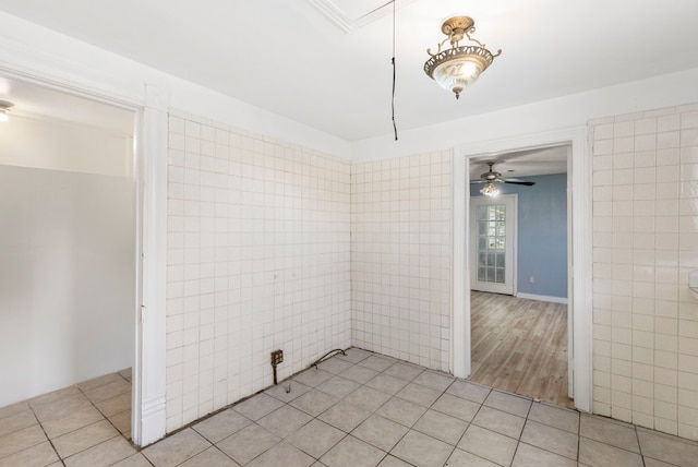 tiled spare room with ceiling fan and tile walls