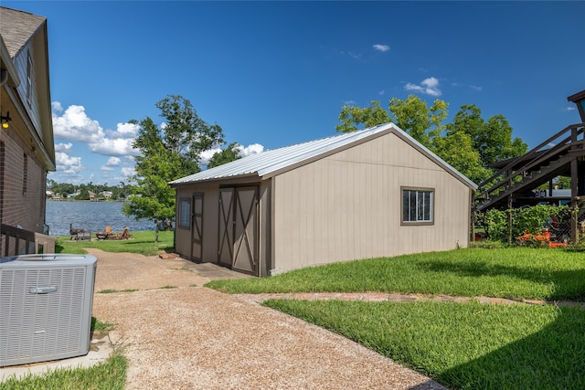 view of side of home with central air condition unit, a lawn, a water view, and a storage shed