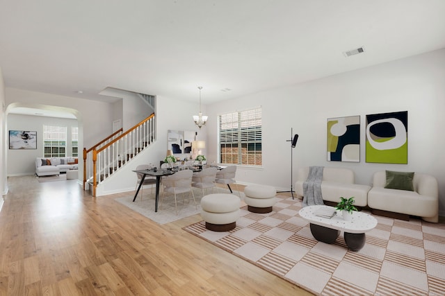 living area featuring light wood-type flooring, visible vents, stairway, arched walkways, and an inviting chandelier