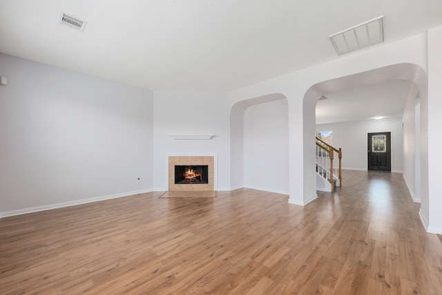 unfurnished living room with light wood-type flooring, visible vents, stairway, and a tile fireplace