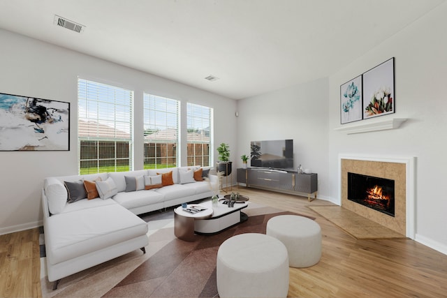 living area featuring a tiled fireplace, visible vents, baseboards, and wood finished floors