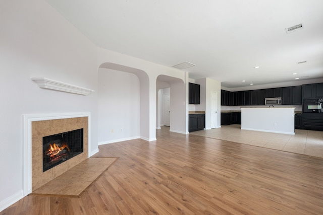 unfurnished living room featuring arched walkways, visible vents, light wood-style flooring, and a fireplace