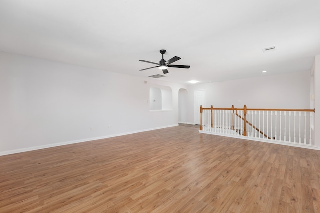 unfurnished room featuring light wood-type flooring, visible vents, a ceiling fan, arched walkways, and baseboards