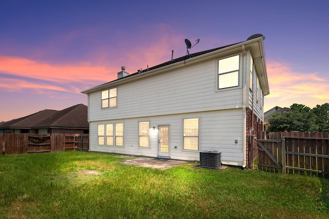 back of house at dusk featuring a gate, cooling unit, a fenced backyard, a chimney, and a lawn