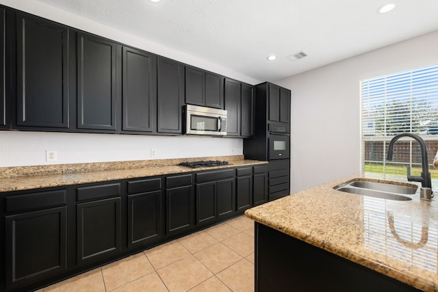 kitchen featuring visible vents, a sink, stainless steel microwave, black oven, and dark cabinetry