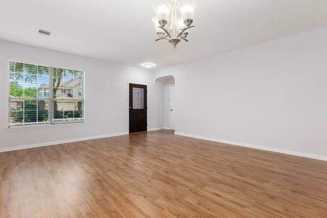 unfurnished room with visible vents, baseboards, light wood-type flooring, arched walkways, and a notable chandelier