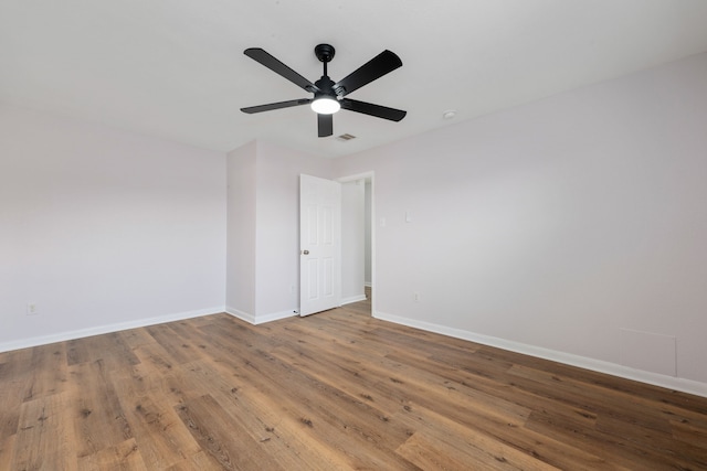 spare room with a ceiling fan, visible vents, wood finished floors, and baseboards