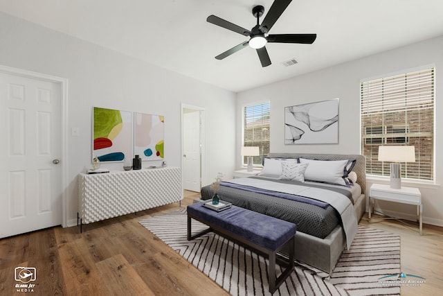 bedroom featuring ceiling fan, wood finished floors, visible vents, and baseboards