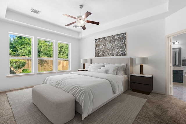 bedroom with a raised ceiling, ensuite bath, and ceiling fan