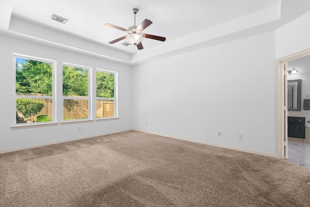 carpeted spare room featuring a raised ceiling and ceiling fan