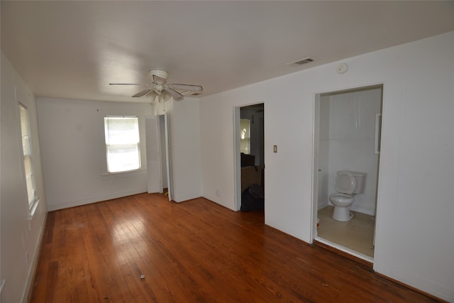 unfurnished bedroom featuring a closet, ensuite bathroom, ceiling fan, and dark wood-type flooring