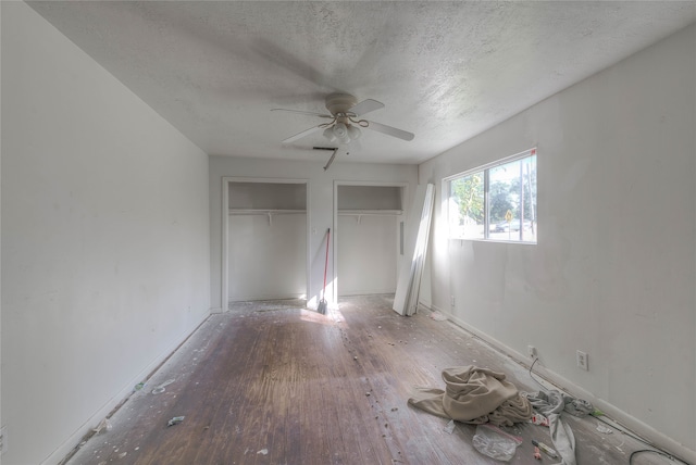 unfurnished bedroom with hardwood / wood-style flooring, ceiling fan, a textured ceiling, and multiple closets