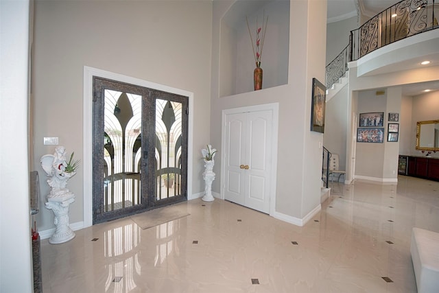 entryway with french doors, a towering ceiling, and ornamental molding