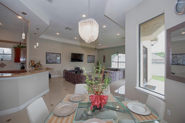 tiled dining space featuring ceiling fan with notable chandelier and a raised ceiling