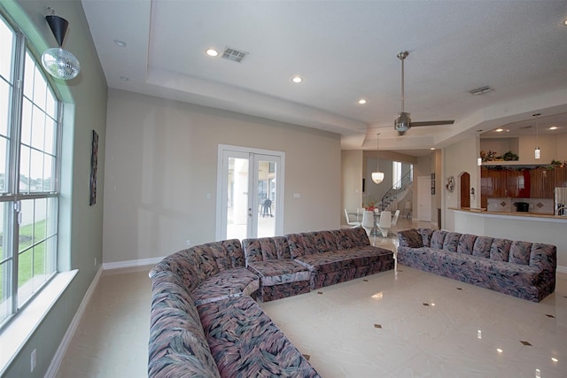 living room featuring ceiling fan, a raised ceiling, and french doors