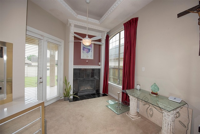 carpeted living room featuring ceiling fan, a tray ceiling, a tile fireplace, and crown molding