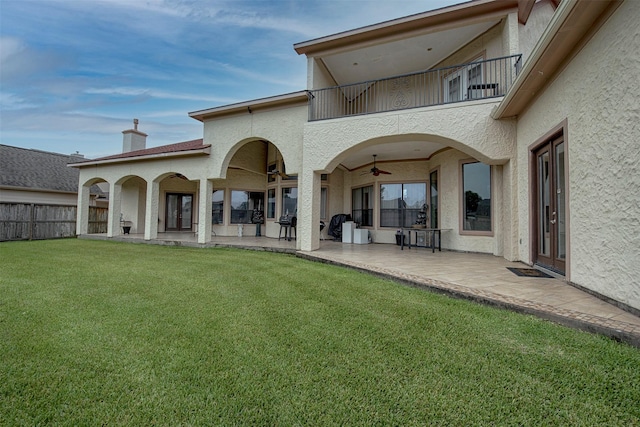 rear view of property with ceiling fan, a lawn, a balcony, and a patio