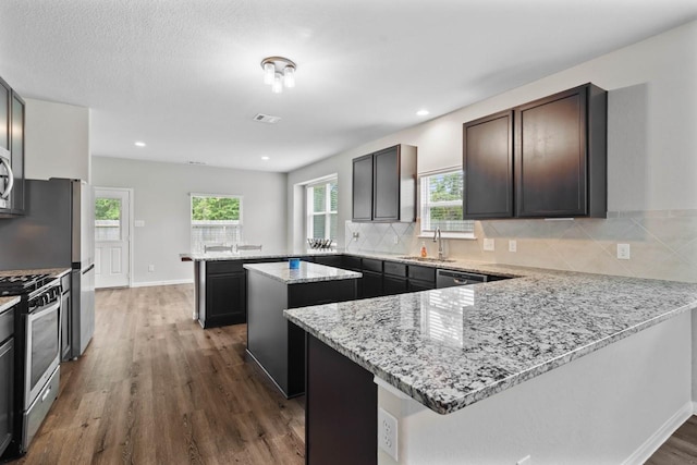 kitchen with appliances with stainless steel finishes, dark hardwood / wood-style flooring, a kitchen island, and plenty of natural light