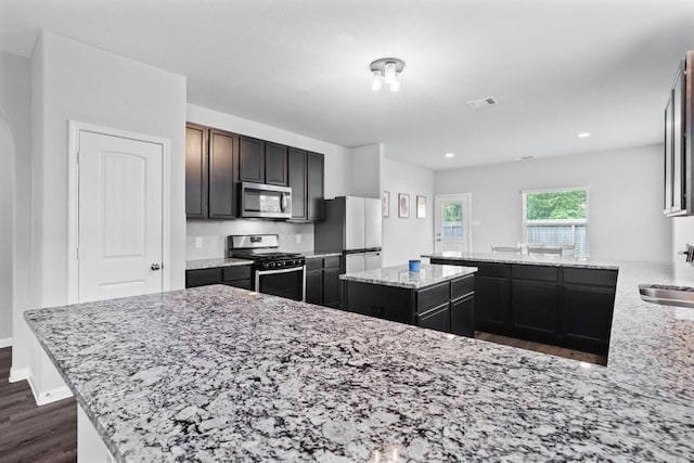 kitchen featuring sink, dark hardwood / wood-style floors, light stone counters, kitchen peninsula, and stainless steel appliances