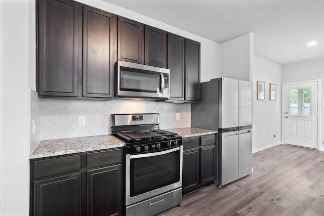 kitchen featuring light stone counters, backsplash, light hardwood / wood-style floors, dark brown cabinets, and appliances with stainless steel finishes