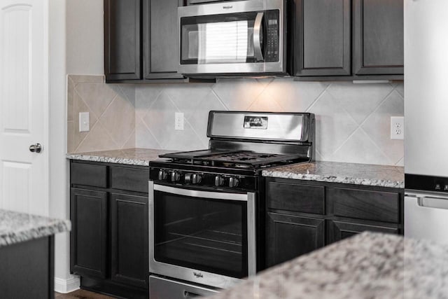 kitchen featuring decorative backsplash, appliances with stainless steel finishes, and light stone counters