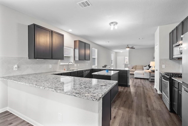 kitchen with kitchen peninsula, a wealth of natural light, stainless steel appliances, and light stone countertops