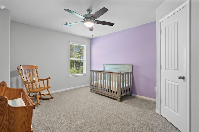 bedroom featuring ceiling fan, a crib, and light carpet