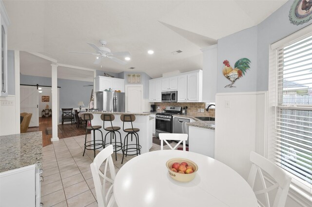 dining space featuring sink, light hardwood / wood-style flooring, ceiling fan, and ornate columns