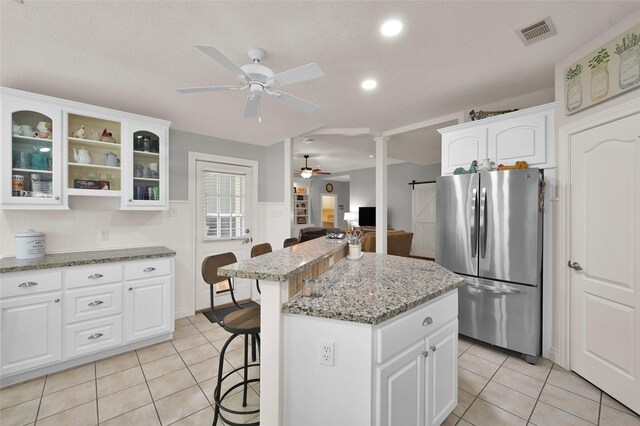 kitchen with stainless steel refrigerator, a center island, white cabinetry, and ceiling fan