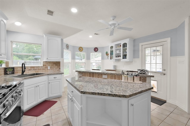 kitchen with light tile patterned flooring, stainless steel gas range oven, sink, and a kitchen island