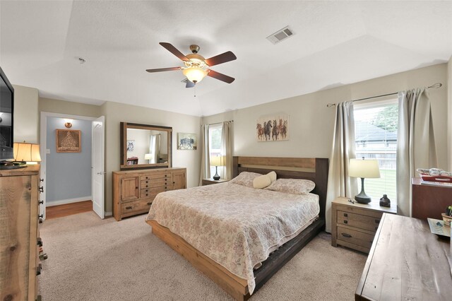 carpeted bedroom with a raised ceiling, multiple windows, and ceiling fan