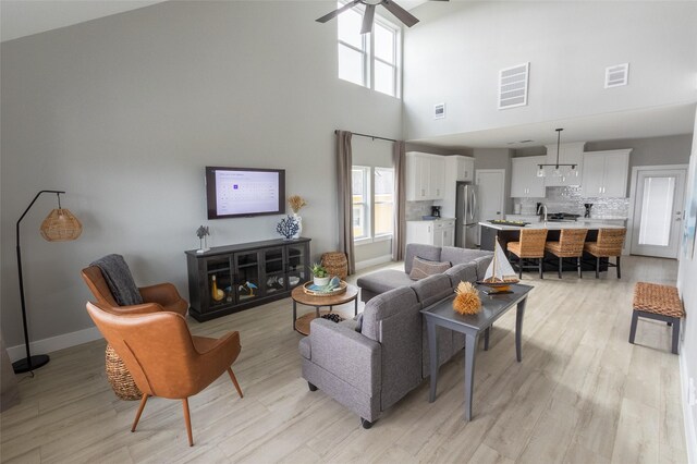 living room with light wood-type flooring, a towering ceiling, sink, and ceiling fan