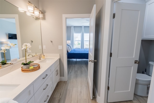 bathroom featuring dual bowl vanity, hardwood / wood-style floors, and toilet