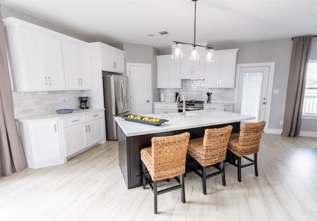 kitchen with white cabinets, a kitchen island with sink, backsplash, and light hardwood / wood-style flooring